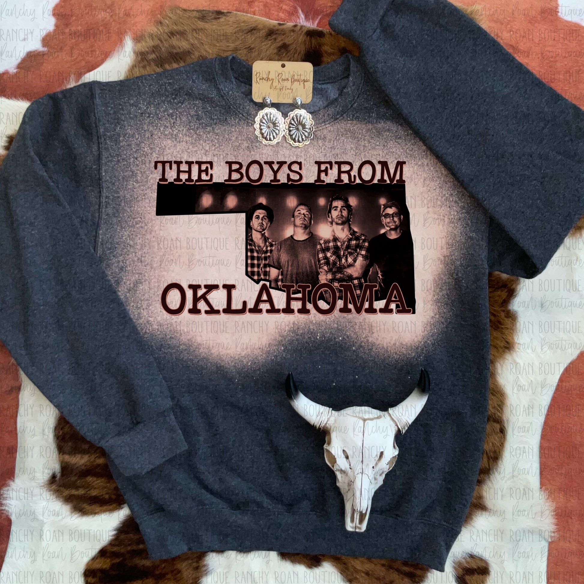  Black Heather unisex crew sweatshirt with the text “The Boys from Oklahoma” featuring a vintage-style graphic of a group of men and a unique bleach splatter design.
