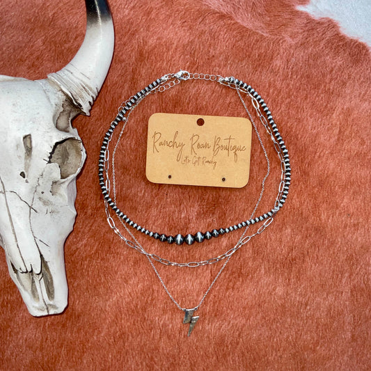 Thunderbolt Layered Navajo Pearl Necklace
 Three-layered Navajo pearl necklace with silver chains and a lightning bolt pendant, featuring a burnished silver finish.