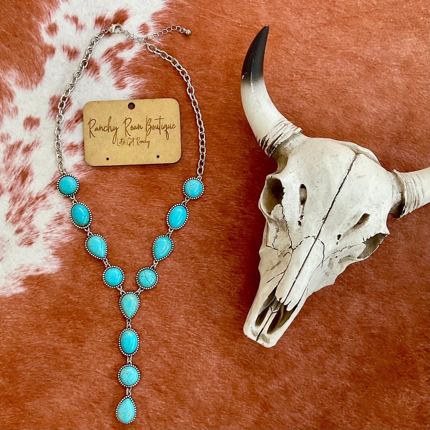 Close-up of Western cabochon stone Y necklace featuring turquoise stones and burnished silver details, displayed with cow skull decor.