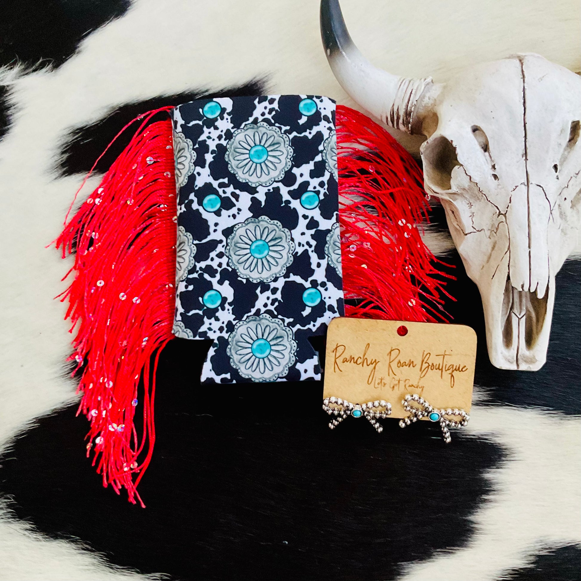 Slim cow print koozie featuring turquoise concho accents with shimmering black fringe detailing.