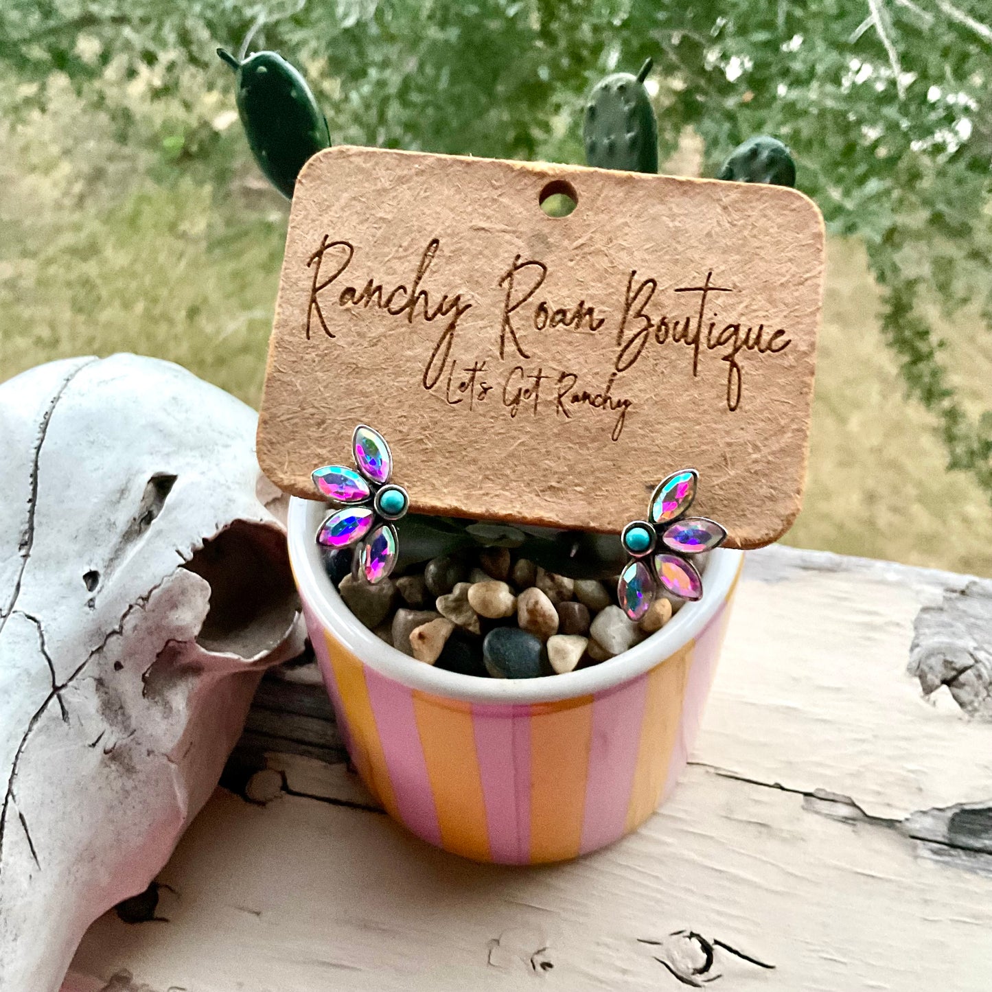 Turquoise and iridescent floral earrings beside a Western skull decor on a rustic surface, capturing the Western aesthetic