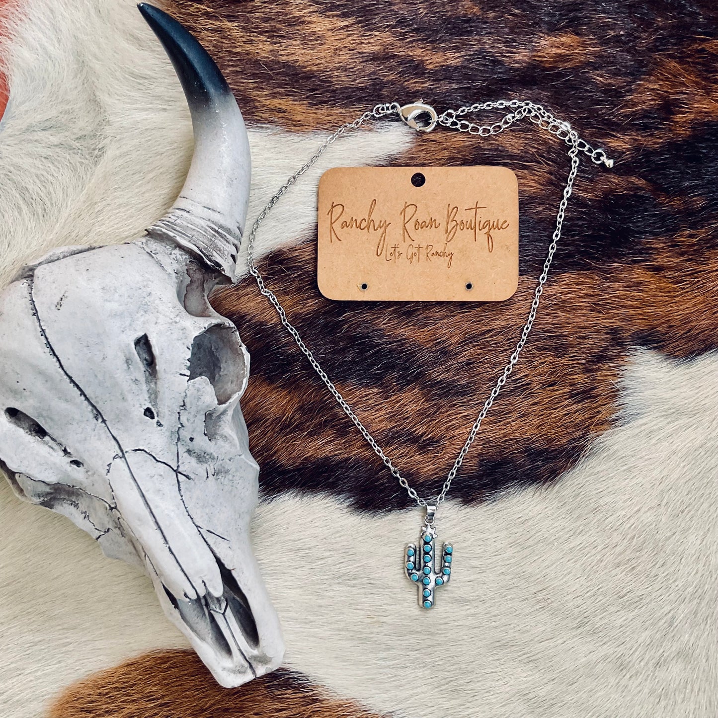 Turquoise cactus pendant necklace photographed on a cowhide background, highlighting its intricate details and rustic charm.