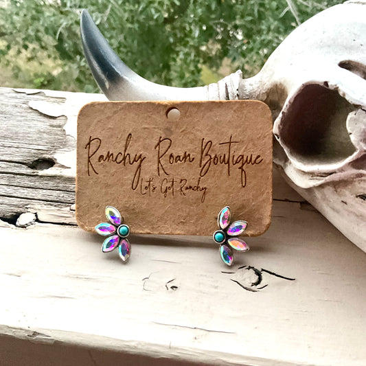 Western-inspired iridescent floral stud earrings with turquoise center on Ranchy Roan Boutique card, styled against rustic decor.