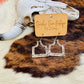 Rustic-themed presentation of cattle tag dangle earrings with a Western aesthetic.
