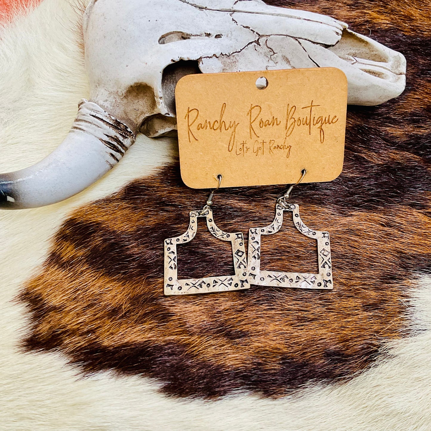 Rustic-themed presentation of cattle tag dangle earrings with a Western aesthetic.