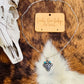 Western Checker Cow Head Necklace displayed on a fur backdrop, featuring a silver-tone pendant with a checker pattern and turquoise details.