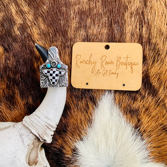  Western Checker Cow Head Cow Tag Cuff Ring displayed on a rich cowhide backdrop with its intricate checkerboard cow head design.