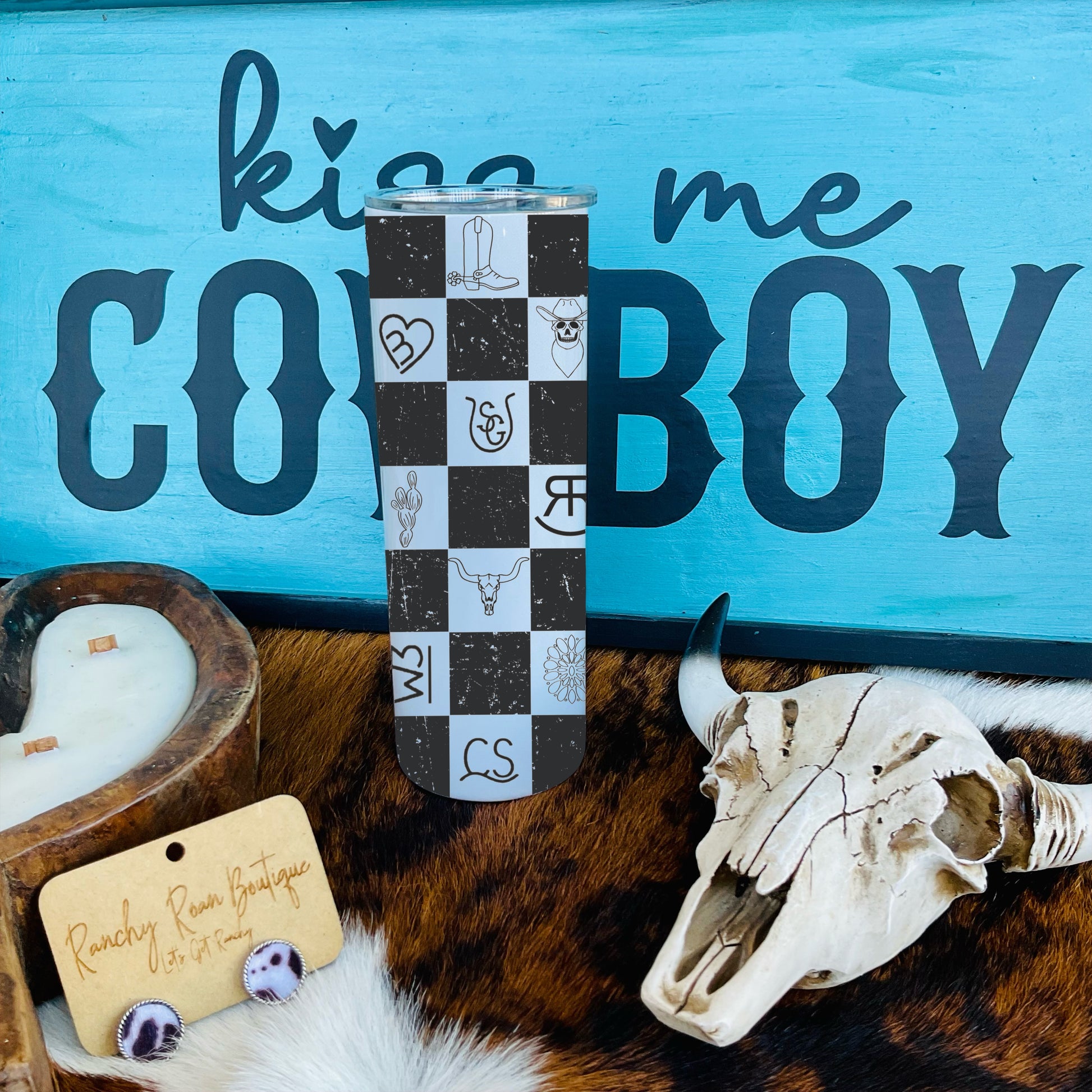 A 20oz stainless steel skinny tumbler with a black-and-white Western checkered pattern, displayed with a clear lid and straw, styled against Western-themed decor.