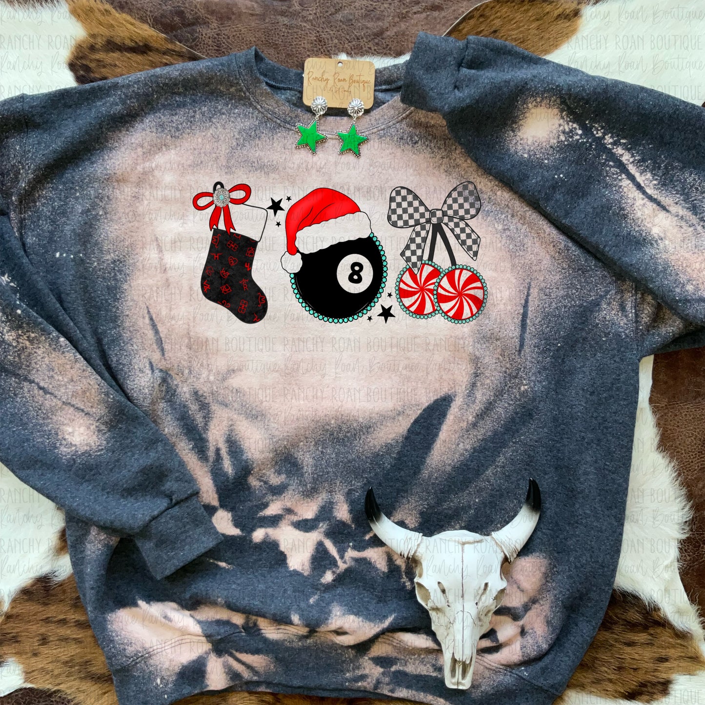 unisex crew sweatshirt featuring a Western Christmas graphic with a stocking, Santa hat, and peppermint candy, displayed with star earrings and a cow skull decor.