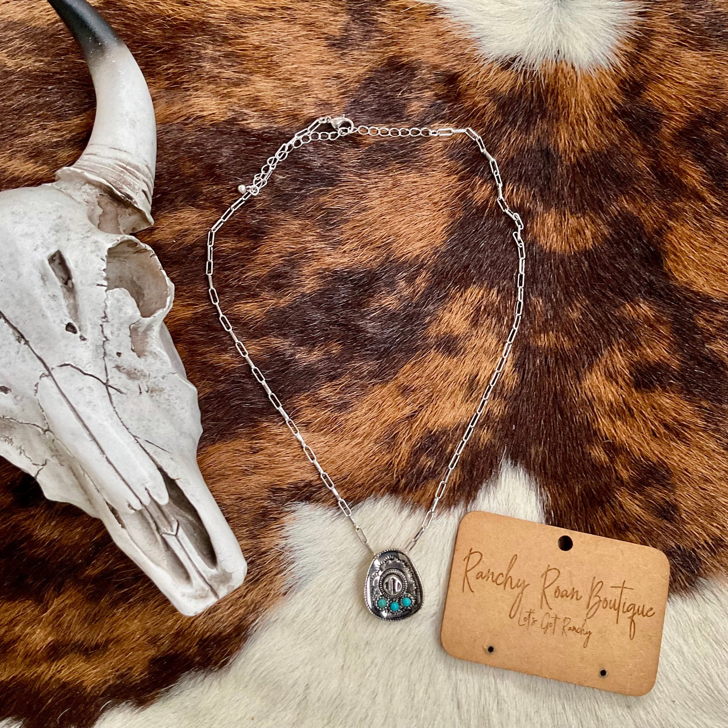 The Western Cowboy Hat Necklace displayed on a cowhide background, showcasing its elegant details and silver chain.