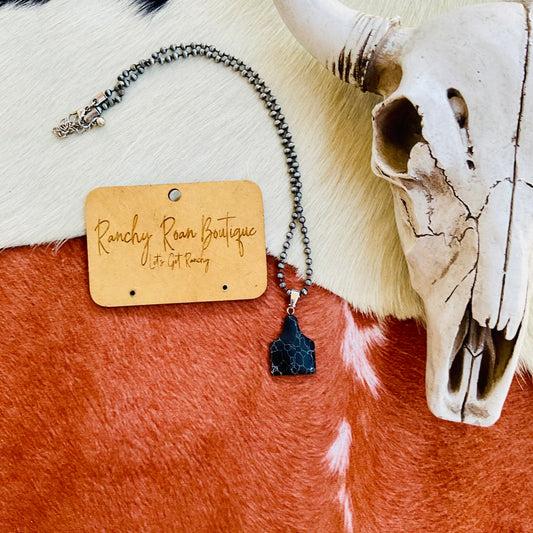 Western Ear Tag Pendant Necklace featuring a black crackled stone pendant on a burnished silver chain, styled with rustic Western accessories.