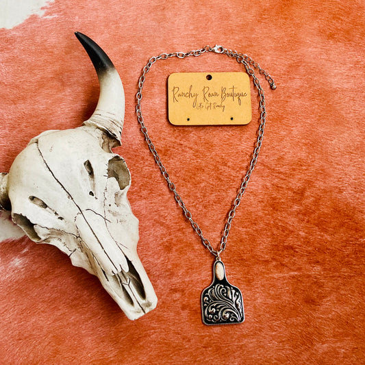 Western cow tag pendant necklace with engraved scrollwork, hanging from an adjustable silver chain, perfect for rodeo and ranch-inspired fashion.