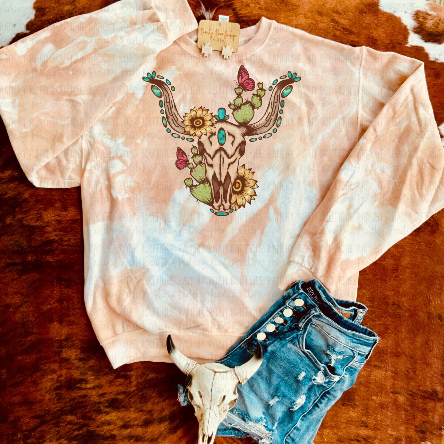 Dyed sweatshirt showcasing a longhorn skull graphic with floral, turquoise, and butterfly accents.