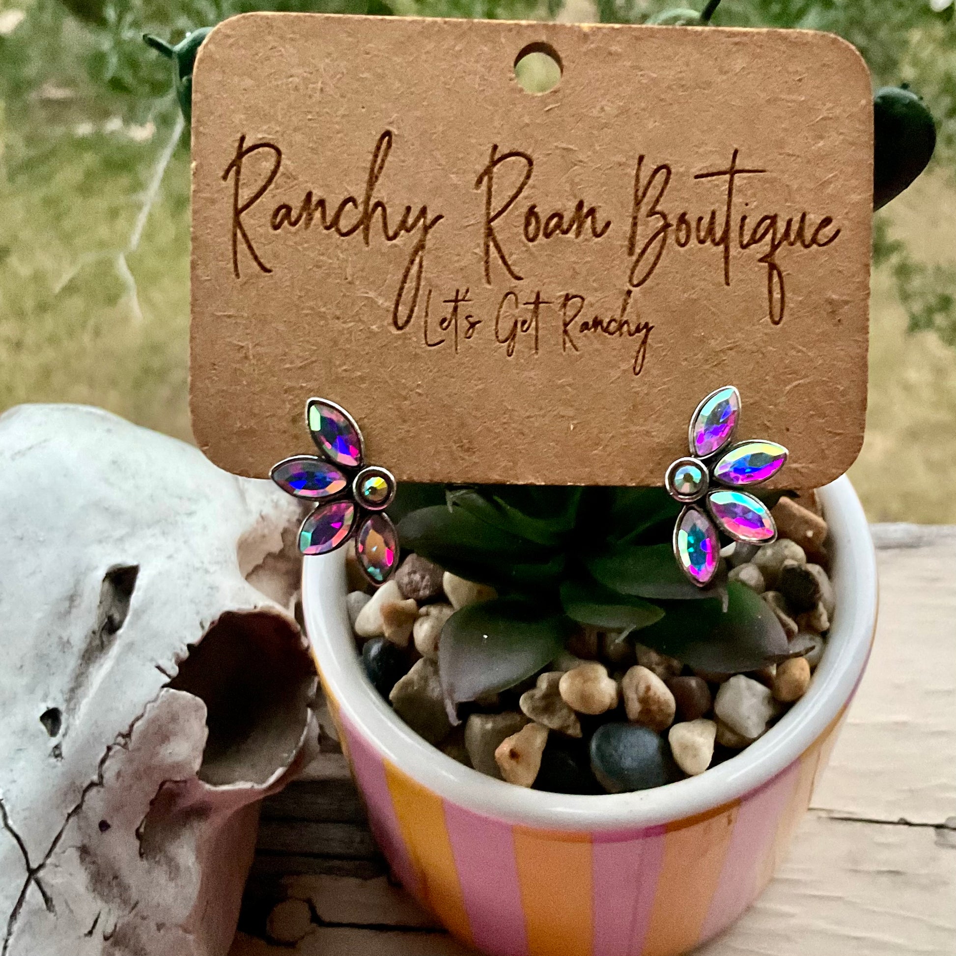 Iridescent floral stud earrings displayed on a potted plant, showcasing a vibrant sparkle against natural greenery.