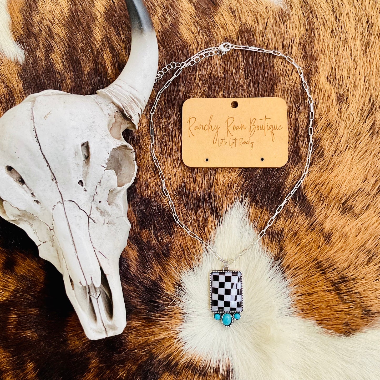 Necklace displayed on a cowhide backdrop, highlighting its bold checker pendant and turquoise accents.