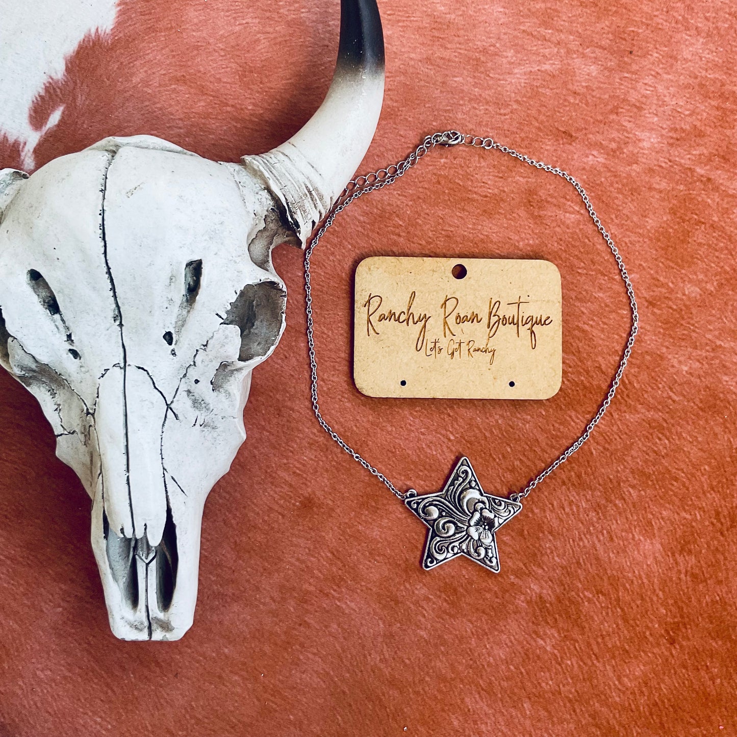 Close-up of a Western star pendant necklace with detailed floral engravings, styled against a Western background