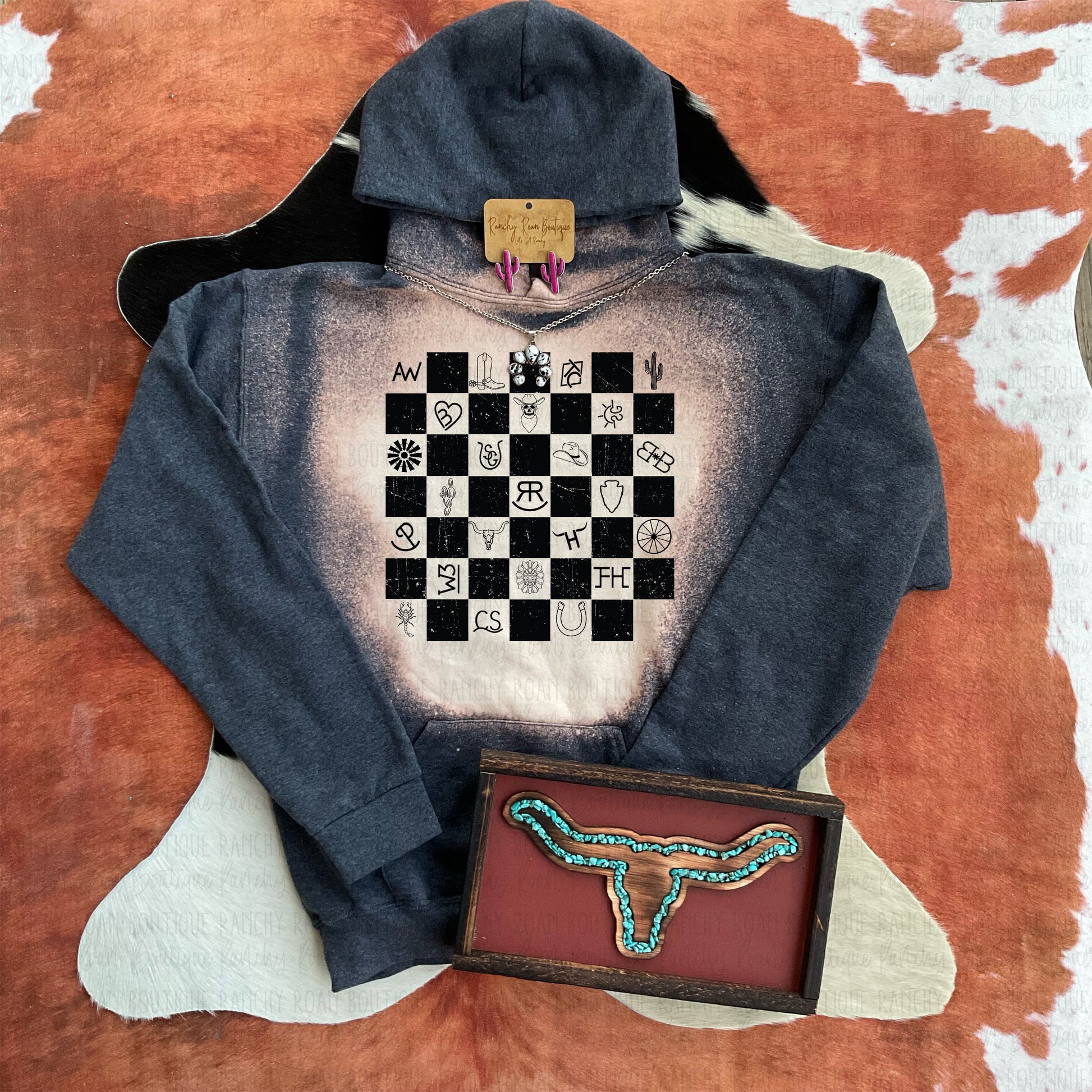 Western Symbols Hoodie displayed with bull skull and turquoise decor on a cowhide rug.