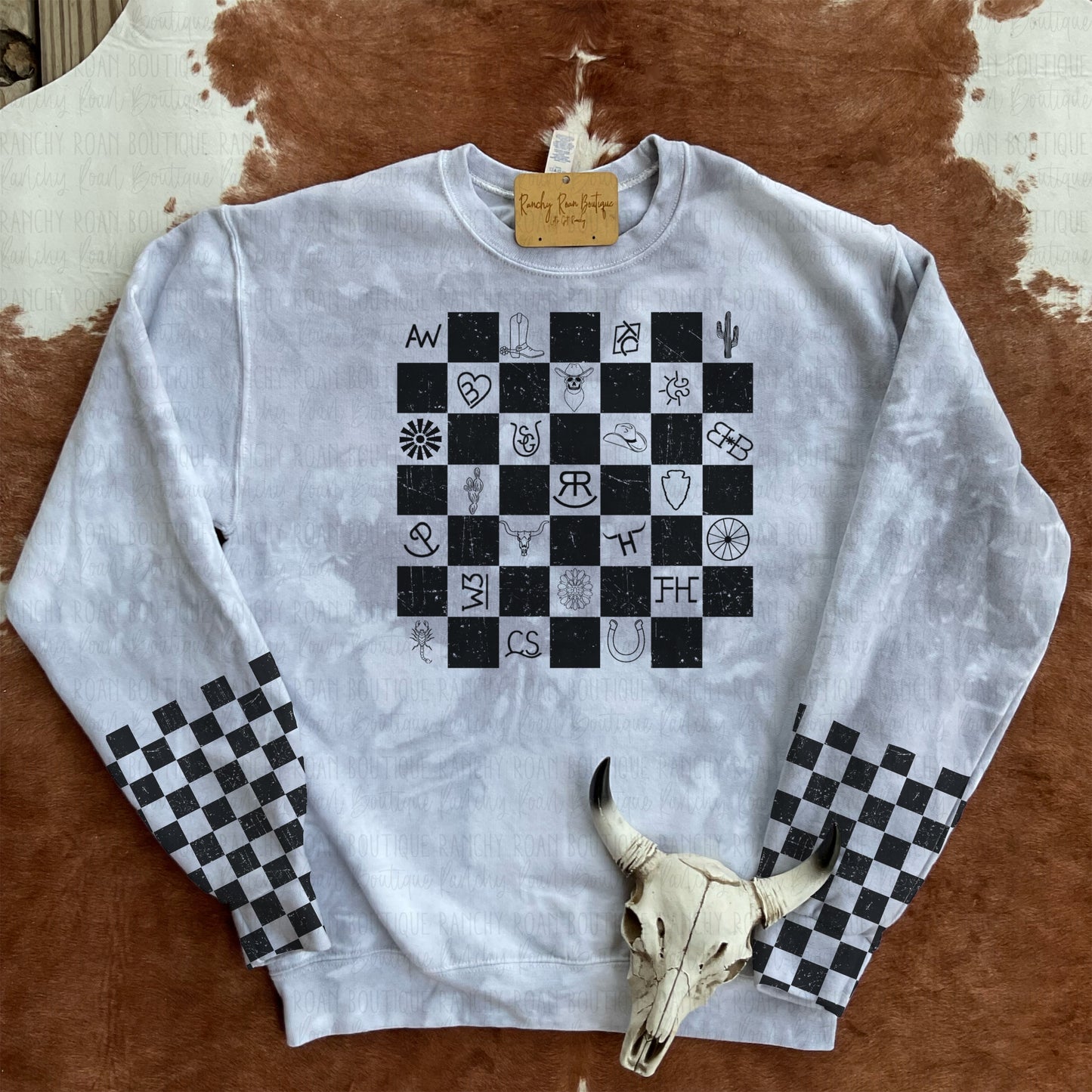 Western Symbols Sweatshirt with checkered sleeves displayed with a bull skull and turquoise decor on a cowhide rug.