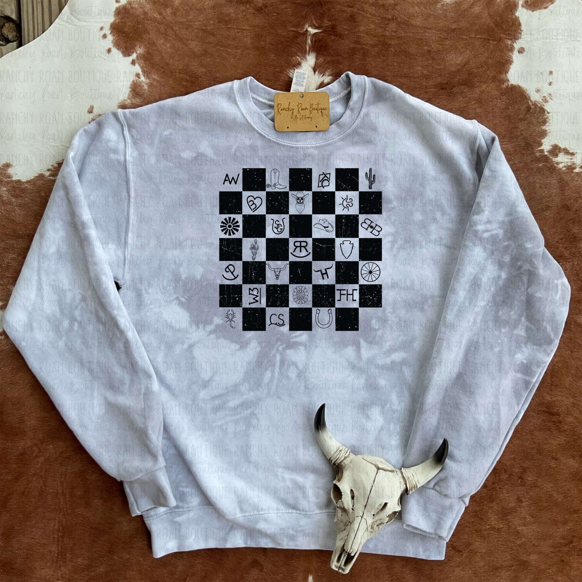 Western Checkered Symbols Sweatshirt displayed with turquoise decor and a bull skull on a cowhide rug.