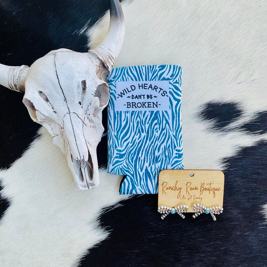  Blue zebra print “Wild Hearts Can’t Be Broken” slim koozie on a cowhide background with Western decor.