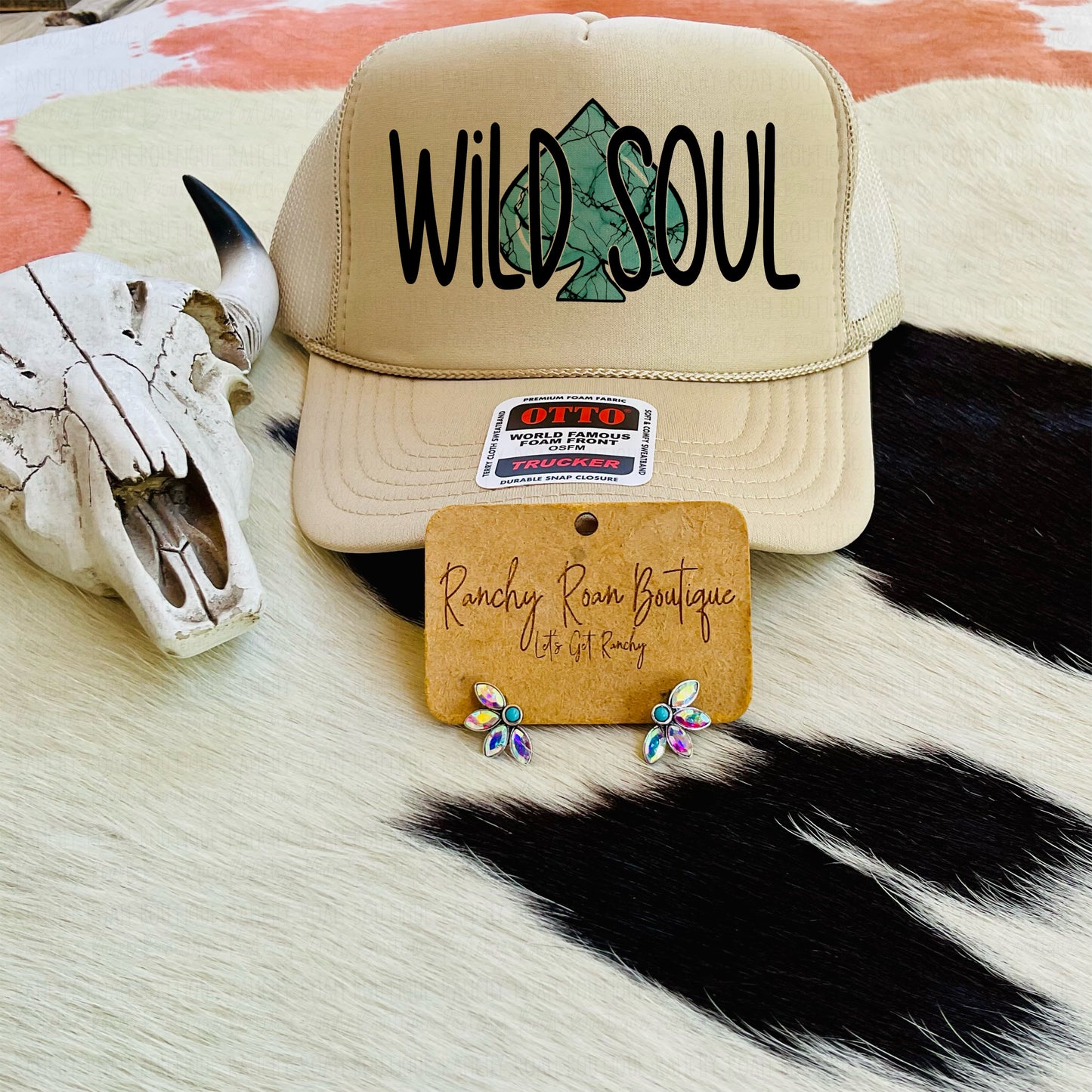  Tan trucker hat with a sage green tree graphic and “Wild Soul” text, displayed with Western-themed background elements.
