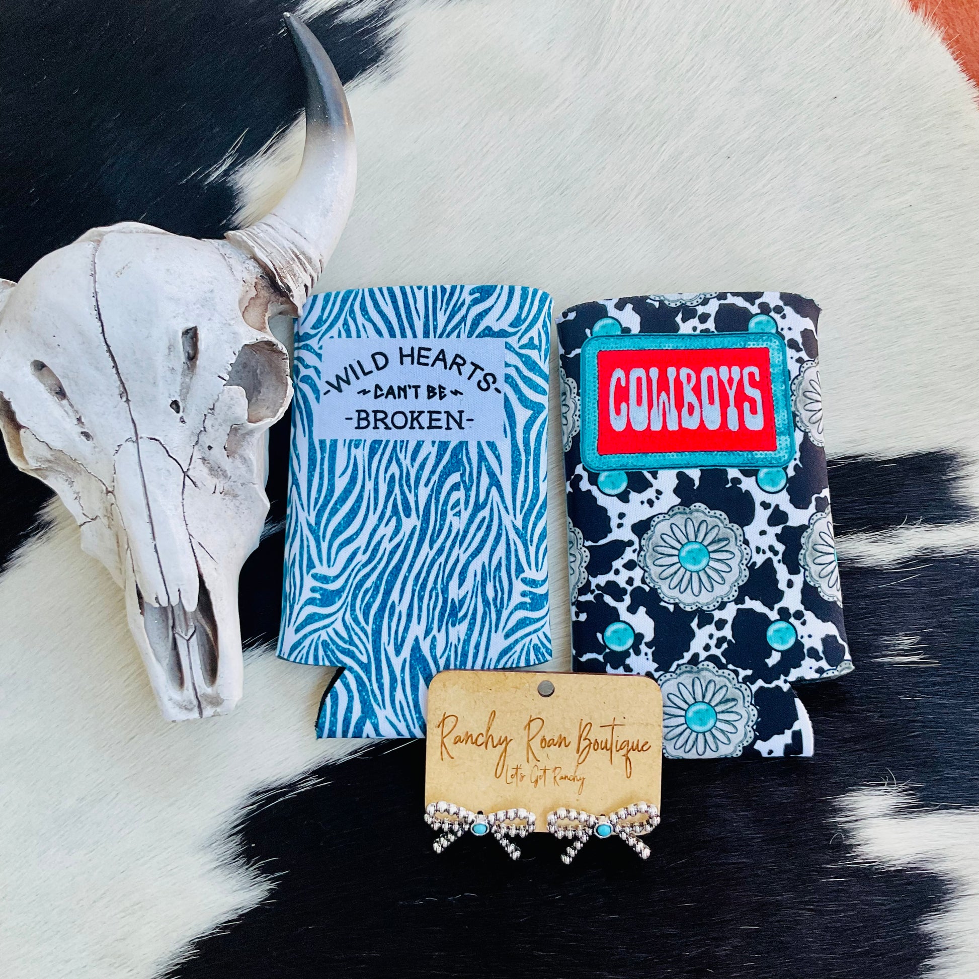 Close-up of the blue zebra print koozie featuring bold text, with earrings and a cow skull prop for aesthetic appeal.
