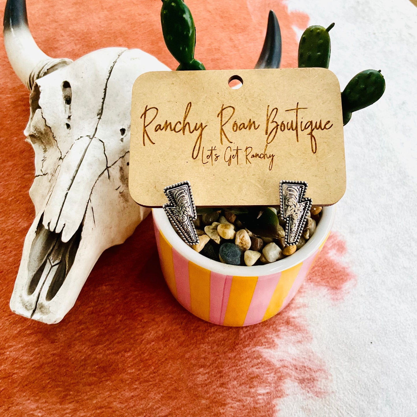 Close-up of lightning bolt-shaped stud earrings with intricate details, styled alongside Western decor on a cowhide background.