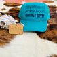 Adjustable turquoise trucker hat featuring a bold Western slogan, displayed on a cowhide background.